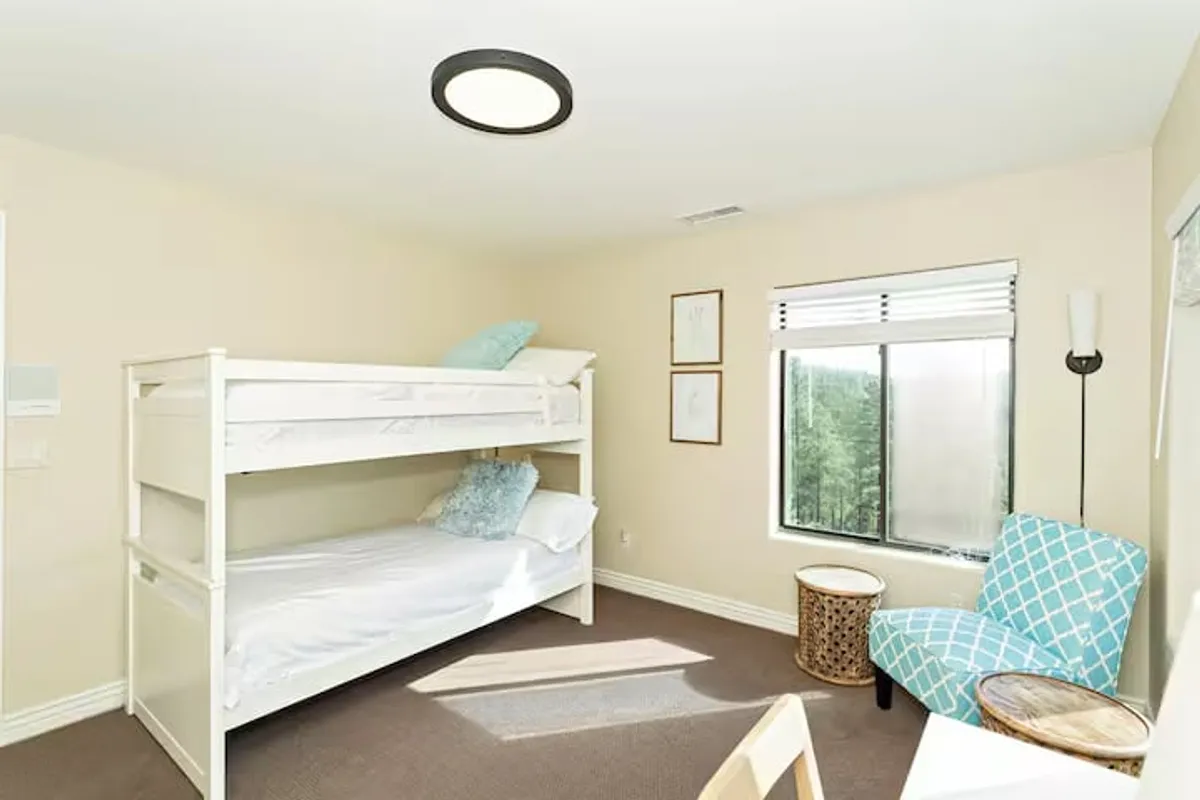 A cozy bunk bed setup is featured alongside an accent chair and a window with a pleasant view. The playful, welcoming vibe is perfect for children or additional guests.