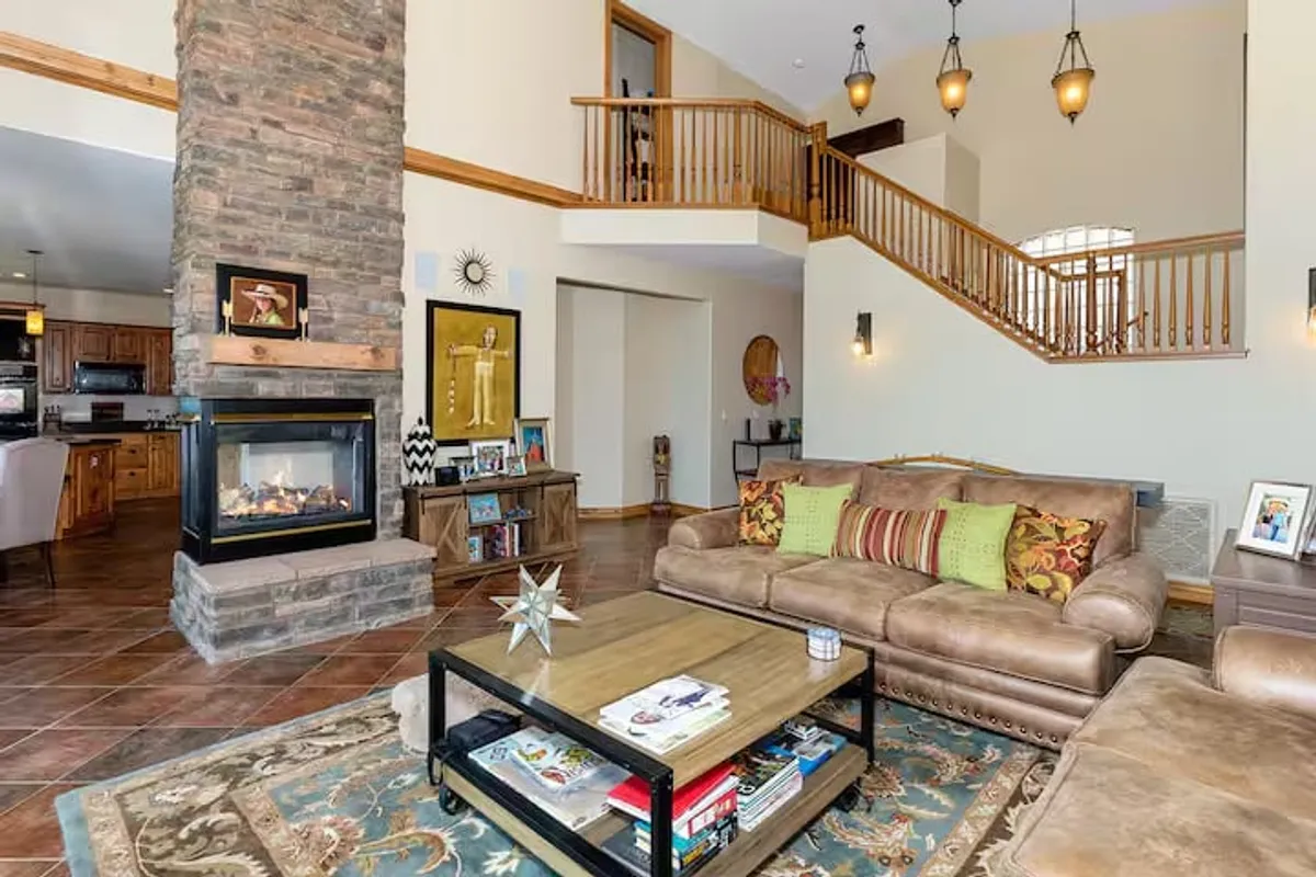 The image showcases a cozy living area in a Prescott single-family home, with a plush sofa facing a glowing fireplace and a coffee table—perfect for game nights or casual gatherings. The space is accented with tasteful holiday decor and features an inviting staircase leading to the upper floors, suggesting a spacious, multi-level retreat ideal for families or groups.