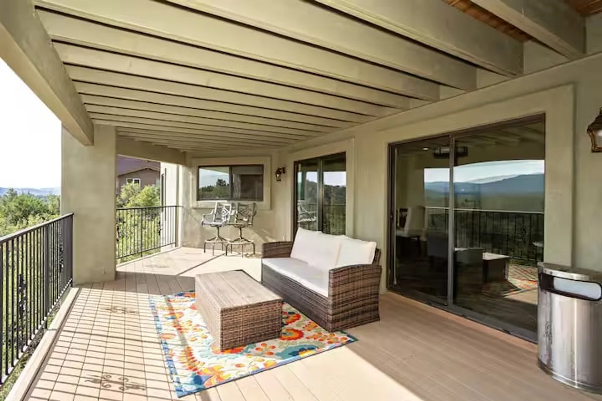 A colorful outdoor seating area is arranged on a patio with a vibrant rug, framed by a panoramic mountain view. The atmosphere is serene and welcoming, inviting guests to enjoy sunsets, social moments, or quiet reflection.