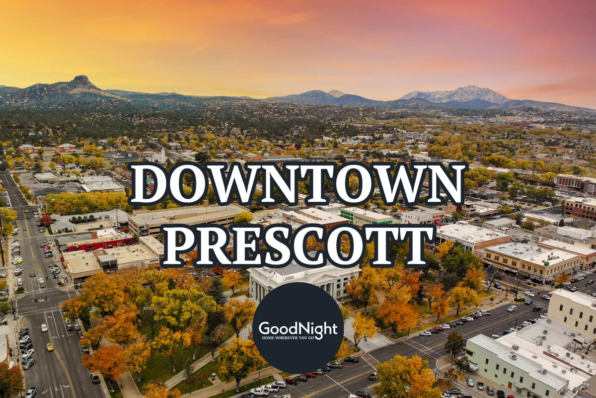 A picturesque view of downtown Prescott showcasing charming downtown buildings, vibrant autumn foliage, and tree-covered mountains in the background. The scene captures the inviting atmosphere of the town and its scenic setting, ideal for exploring shops, cafes, and cultural events.