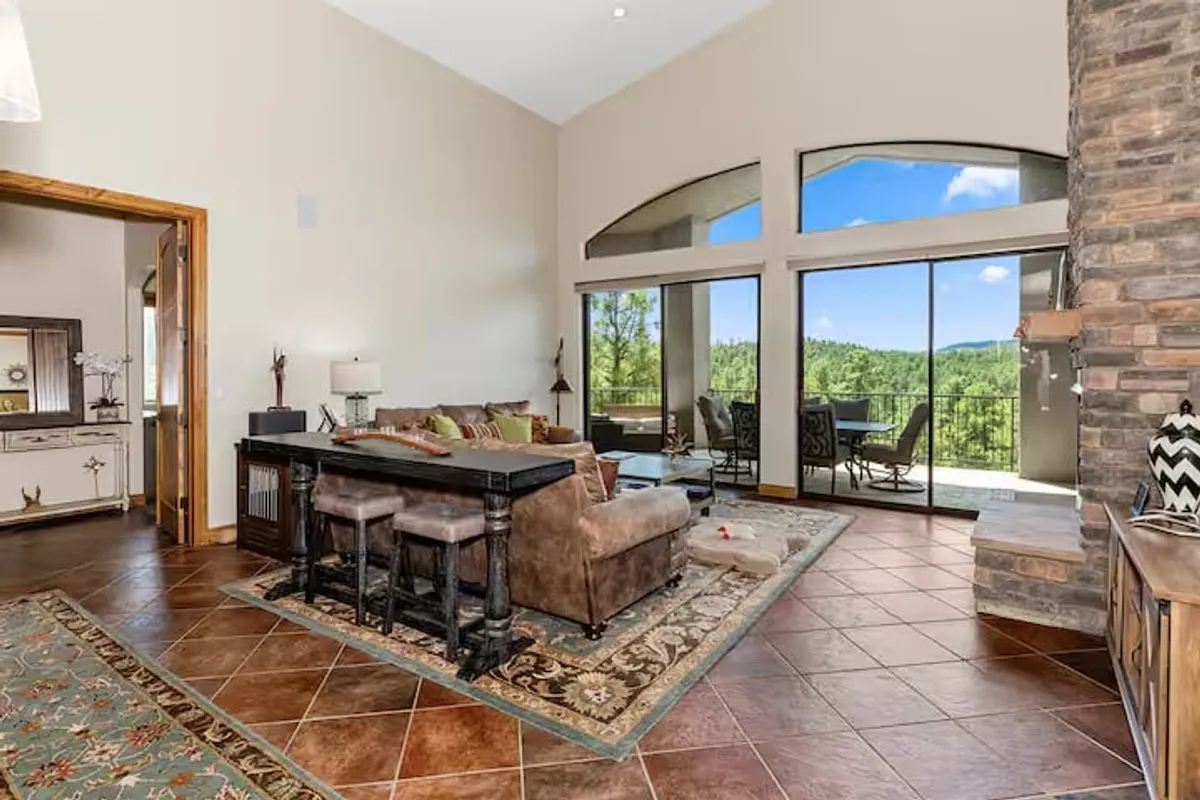A cozy living room featuring large windows with scenic views, a comfortable seating area, a decorative rug, and a fireplace. The arrangement is ideal for socializing, relaxing, and celebrating special moments.