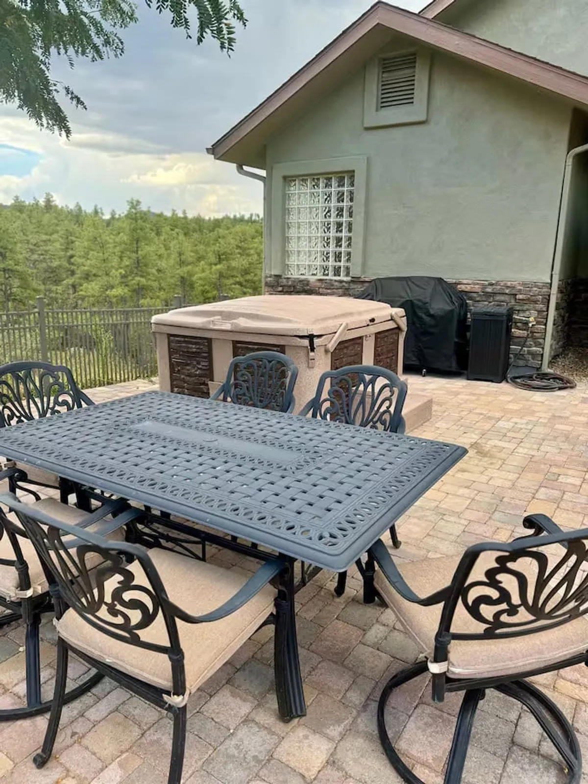 A spacious patio area features both a dining table and a hot tub, set against a backdrop of lush greenery. The space is designed for both relaxation and socializing, inviting guests to enjoy meals, soak in the hot tub, and connect with the outdoors.