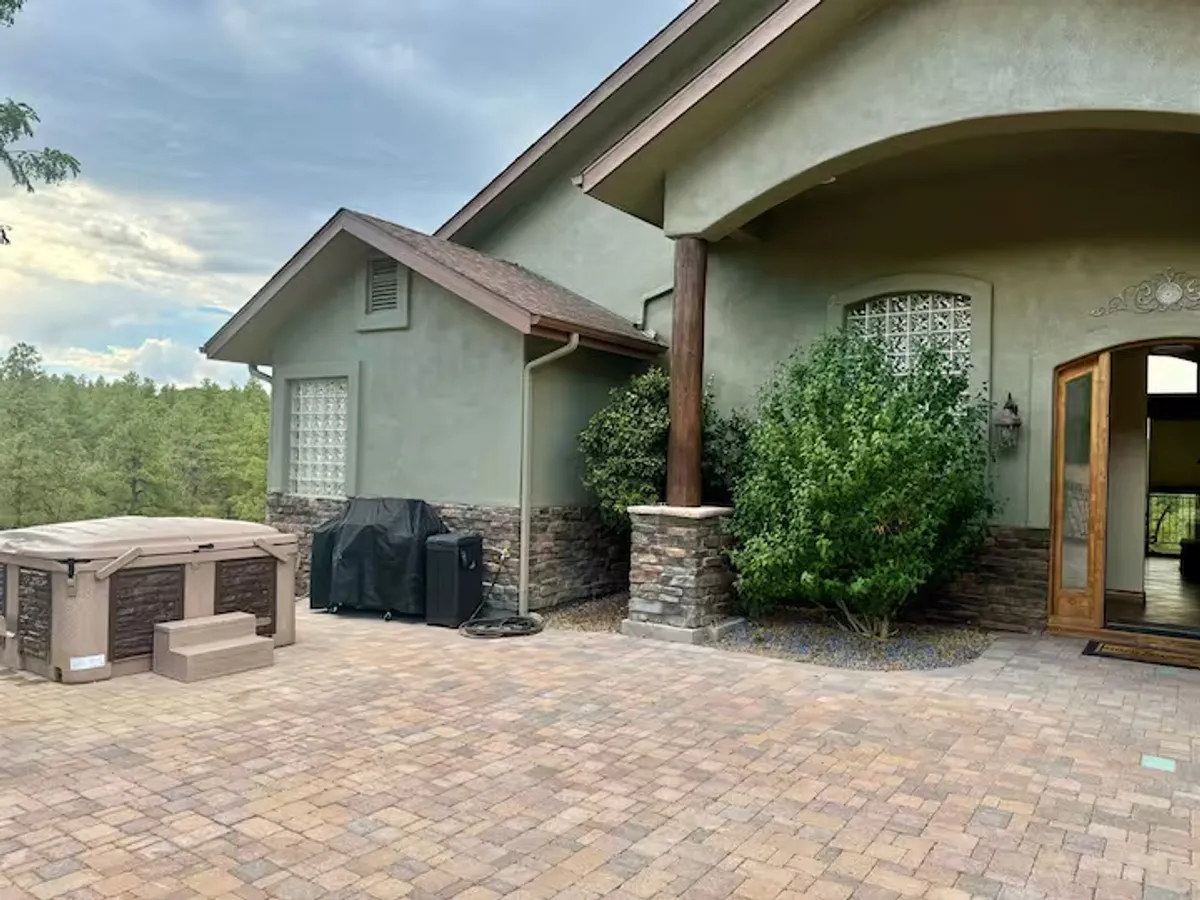 The home’s inviting outdoor hot tub sits beside the entrance, framed by stone pillars and landscaping. Surrounded by greenery, this setting offers a serene place to unwind, with glimpses of mountain scenery and the promise of relaxation after a day outdoors.