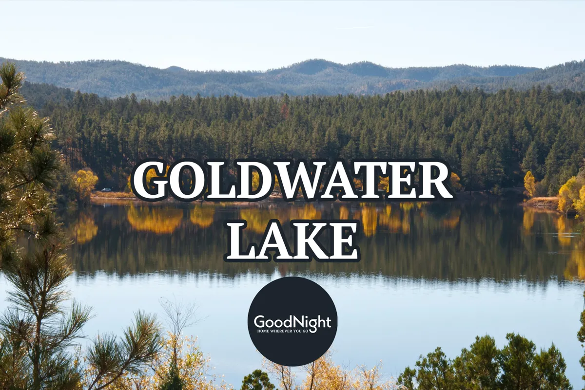 This image captures the tranquil expanse of Goldwater Lake, bordered by lush trees and mountainous terrain. Reflections shimmer on the water's surface, conveying the peaceful atmosphere and abundant natural beauty of the Prescott area. The open lake, framed by forested hills, is ideal for water activities like kayaking, fishing, and picnicking.