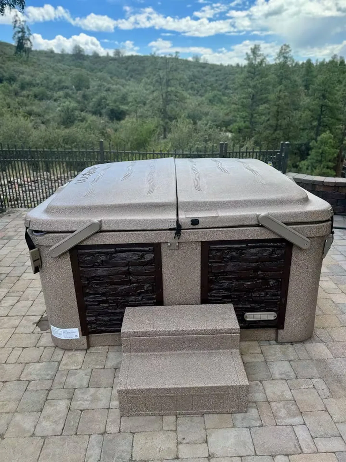 A bubbling hot tub is nestled outdoors, surrounded by a serene landscape and natural elements. Steps lead up to the hot tub, which is positioned to offer views of the surrounding area, making it ideal for relaxation beneath the open sky.